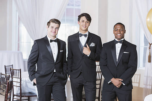 Three young men wearing tuxedos A group of three multi-ethnic young men wearing tuxedos, standing in a row, smiling at the camera. They are at a party, prom, a wedding or some other special formal event. tuxedo stock pictures, royalty-free photos & images