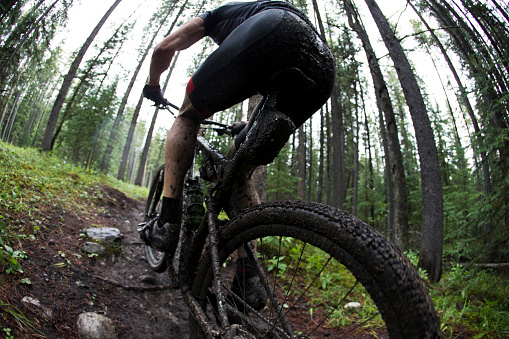 A man competes in a mountain bike race on a wet and muddy course in the rain.