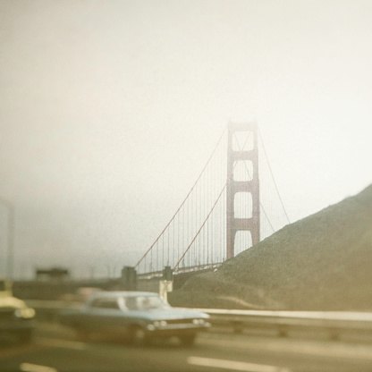 Cars driving on the highway with the Golden Gate Bridge in a foggy background.