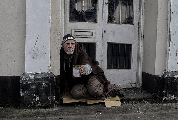 Homeless man in doorway  holding out a tin hoping to receive money from passers by