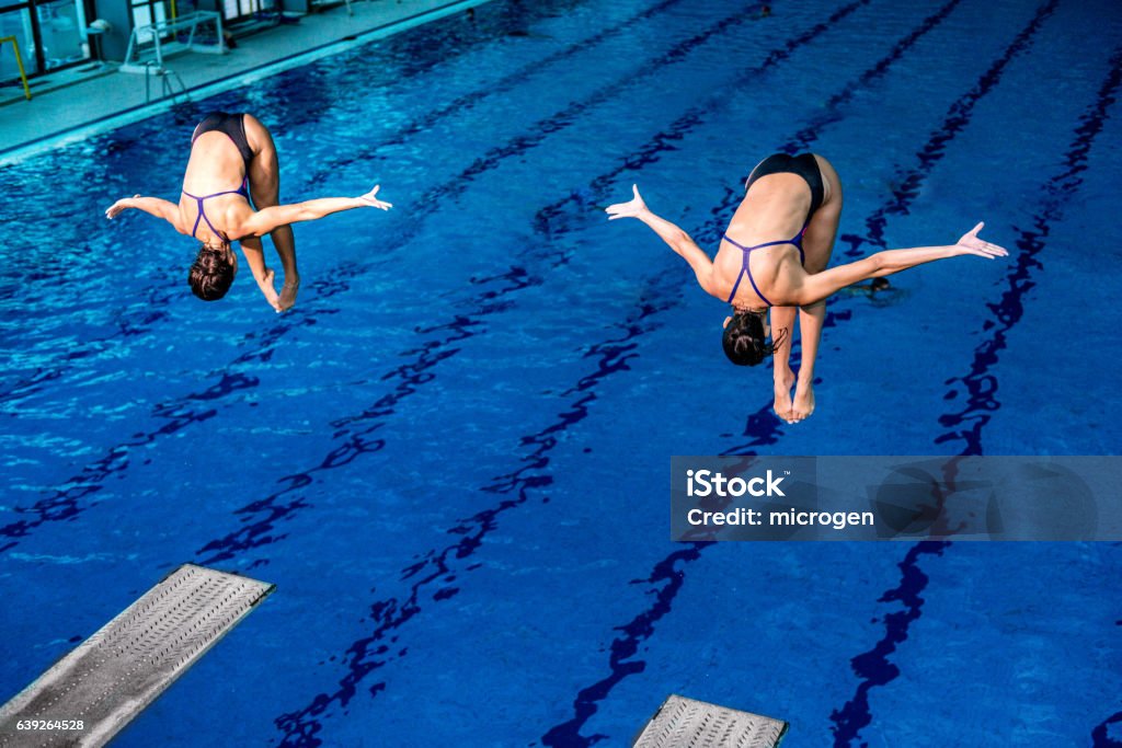 Synchronized diving Synchronized diving. Two female springboard divers in the air Diving Into Water Stock Photo