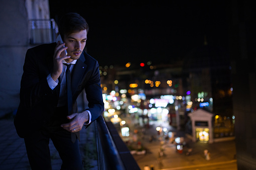 Businessman using phone.Night.businessman working late into the night.In the town are the lights because the night.Businessman on top of the building using telephone