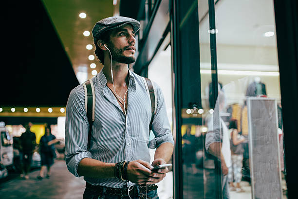 Taking a night walk Handsome Mantaking a walk by the shopping mall outdoors, at night. He is listening music on headphones. mall walker stock pictures, royalty-free photos & images