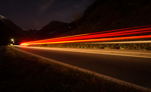 The headlights and taillights of passing cars light up the darkness of an alpine valley.