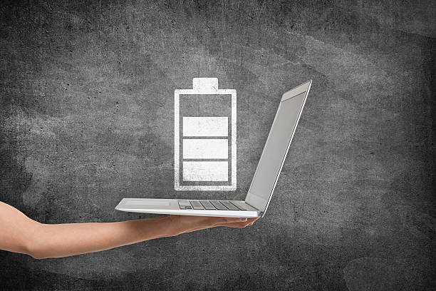 Businesswoman holding laptop under battery charging icon on blackboard