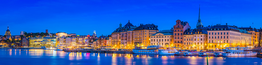 Clear blue summer skies framing the colourful lights and iconic historic townhouses, hotels, restaurants and bars of Gamla Stan reflecting in the tranquil waters of Stockholm, Sweden's vibrant capital city.