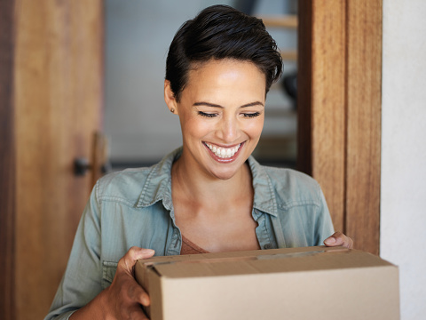 Shot of a smiling young woman standing at her front door receiving a package from a courier