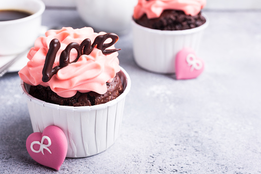 Beautiful chocolate cupcake, pink cream and heart on gray stone background. Valentines, Mother Day, wedding concept with copy space.