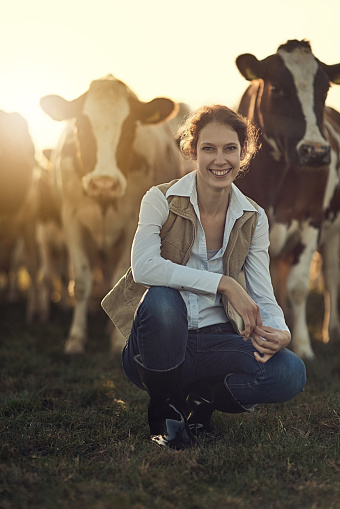 Portrait of a happy female farmer posing in front of her herd of cattle