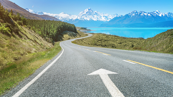 Panorama of the road to Mount Cook along the turquoise Lake Pukaki with an forward pointing arrow country road marking. South Island, Canterbury, Mount Cook, Lake Pukaki, New Zealand