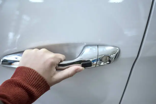 Female hand holding silver doorhandle a white car