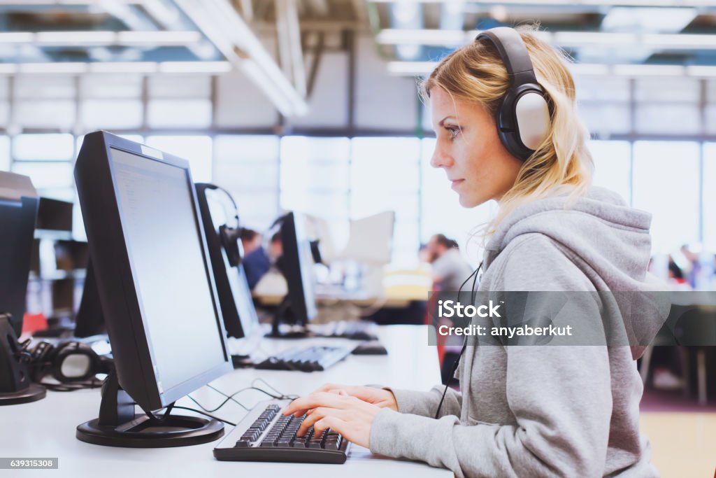 Erwachsenenbildung, Student in Kopfhörern arbeiten am Computer in der Bibliothek - Lizenzfrei Schulische Prüfung Stock-Foto