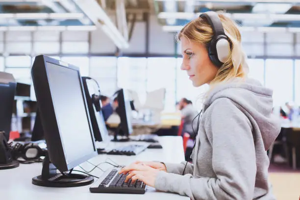 Photo of adult education, student in headphones working on computer in library