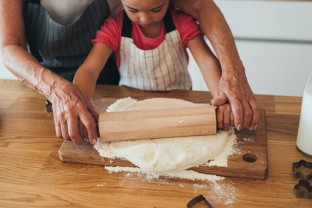 祖母は彼女の孫娘に生地をロールアウトするように教える - grandmother domestic life cooking domestic kitchen ストックフォトと画像