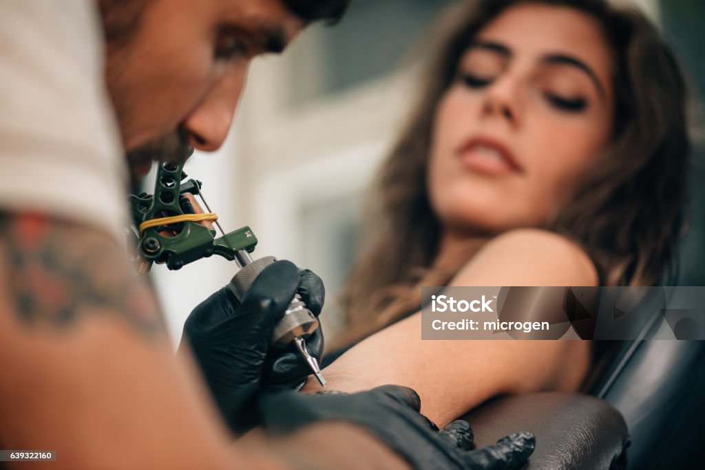 Tattooing Tattoo artist creating a tattoo on a girl's arm. Focus on tattoo machine Tattooing Stock Photo
