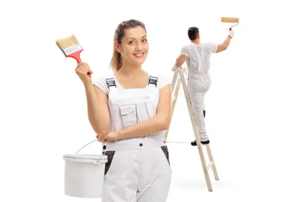 Female painter holding a color bucket and a paintbrush with a male painter painting climbed up a ladder isolated on white background