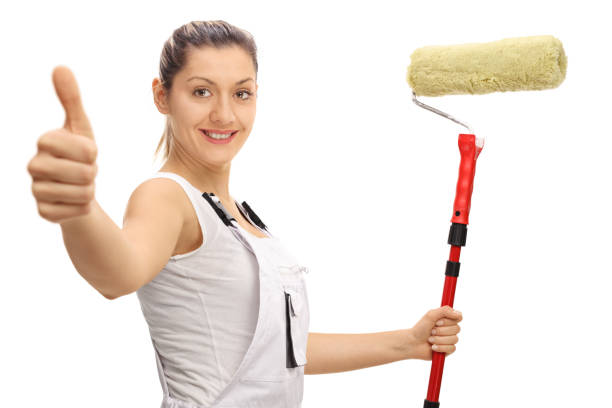 istock Delighted female painter holding paint roller and giving thumb u 639336132