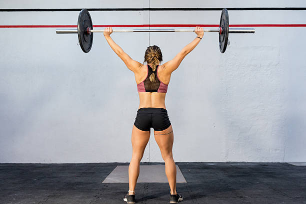 Weight training at gym ! Horizontal rear view color image of muscled woman training at gym with heavy barbell. back shoulder tattoos for women pictures stock pictures, royalty-free photos & images
