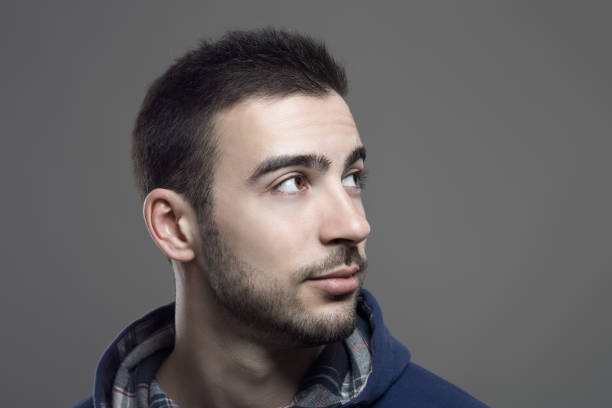 Profile view of young man looking away with blank facial expression on a white background. Horizontal composition. Studio shot.