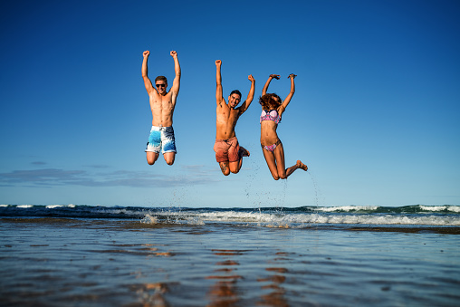 Friends on the beach jumping in the air.