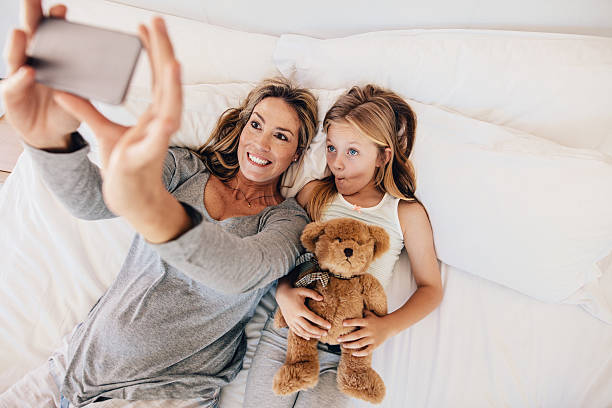 istock Mother and daughter lying on bed and taking selfie 639355726