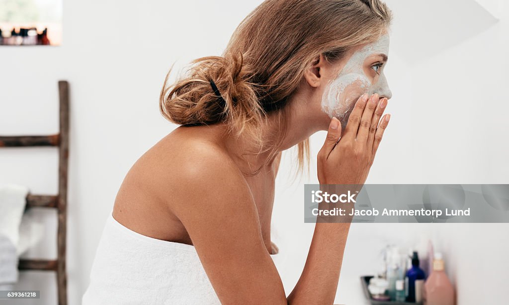 Woman taking care of her facial skin Side view shot of young woman applying facial cosmetic mask in bathroom.  Female taking care of her face skin. Facial Mask - Beauty Product Stock Photo