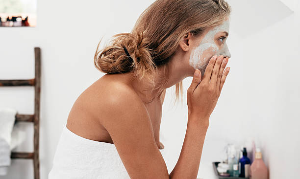 Woman taking care of her facial skin Side view shot of young woman applying facial cosmetic mask in bathroom. Female taking care of her face skin. woman wrapped in bath towel stock pictures, royalty-free photos & images