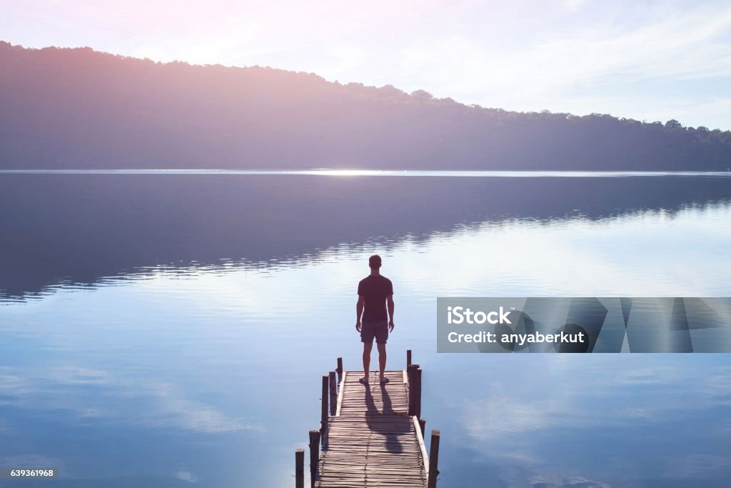 human strength or psychology concept, man standing on pier dreamer, silhouette of man standing on the lake wooden pier at sunset, human strength, psychology concept Change Stock Photo