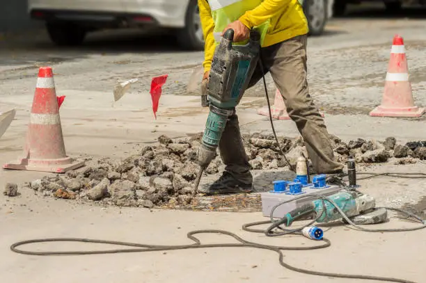 Worker drilling concrete driveway with jackhammer. Man repairing road surface with heavy duty machine.