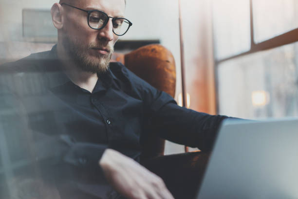 istock Sad bearded businessman working in modern loft office. Man using 639368170