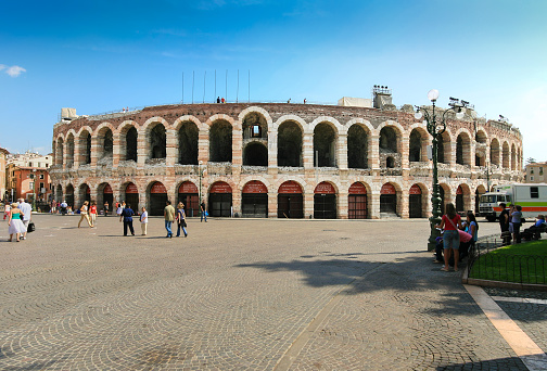 Verona, Italy - September 6, 2008: Verona Arena, Tourists and Piazza Bra, Verona, Italy. The Verona Arena (Arena di Verona) is a Roman amphitheatre built in the first century. It is still in use and is famous for the large-scale opera performances given there. It is one of the best preserved ancient structures of its kind. In ancient times, about 30,000 people was the capacity of the Arena. Sightseeing tourists, truck and vivid blue clear sky with some clouds are in the image.