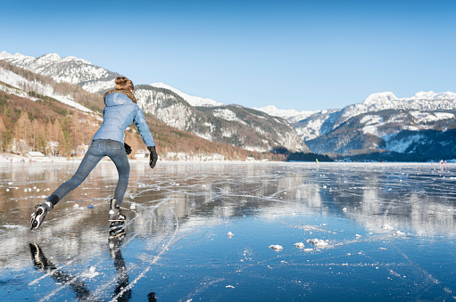 Beautiful woman ice skating on the frozen lake Grundlsee in front of a stunning Alps panorama. Nikon 810. Converted from RAW.