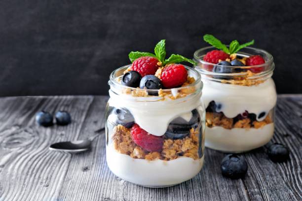 istock Blueberry, raspberry parfaits in mason jars, scene on dark background 639376284