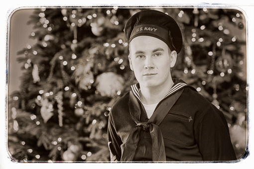 WWII US Navy Sailor home for the holidays.  He is dressed in an authentic uniform for the period.  Aged photo.  Vintage Style.