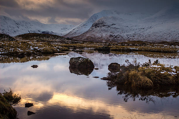 Snow capped mountains coming down to meet the still water of Loch Nah-Achlaise on Rannoch Moor, near Glencoe in the Scottish Highlands.