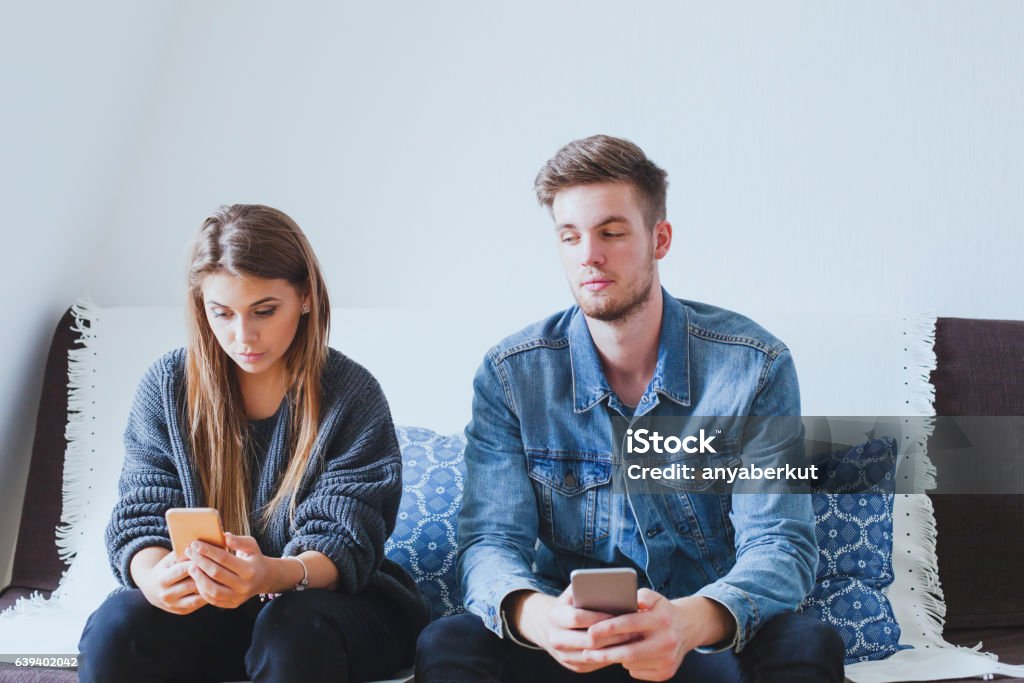 jealous man husband spying wife, suspicious boyfriend jealous man husband spying wife, suspicious boyfriend trying to read messages on the mobile phone of his girlfriend while she is not watching Infidelity Stock Photo