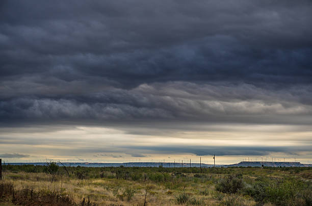 Beams of sunlight shine down through the storm clouds passing over the West Texas plain, with wind turbines on a distant ridge.