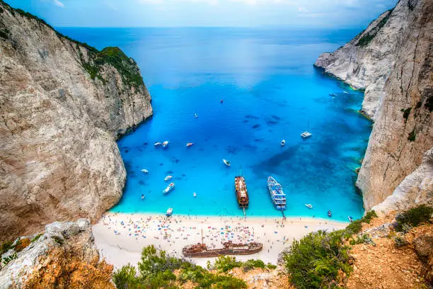 Tourists and tourist boats  in the famous Navagio Bay, Zakynthos island, Greece. The beach of Navagio with the old shipwreck is one of the main tourism spots of Zakynthos island in Greece - beside of the wreck its the turquoise sea what makes this place so famous.