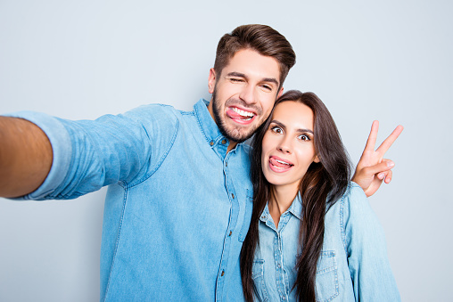 Funny couple showing tongues and gesturing v-sign while making selfie