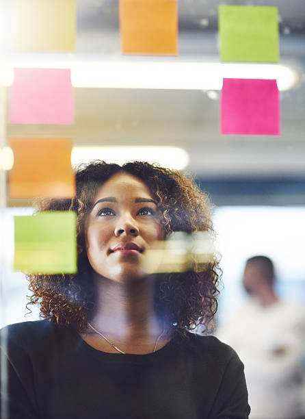 Thinking critically to create success Shot of a young woman having a brainstorming session with sticky notes at work paper stock stock pictures, royalty-free photos & images