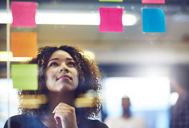 Let your brain be your best friend when problem solving Shot of a young woman having a brainstorming session with sticky notes at work Career Planning stock pictures, royalty-free photos & images