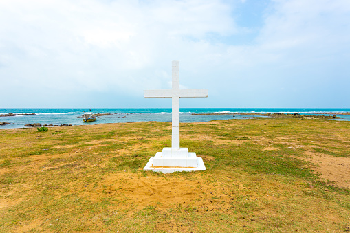White cross is planted outside of Saint Thomas Church along the ocean in Point Pedro, Jaffna, Sri Lanka. Horizontal