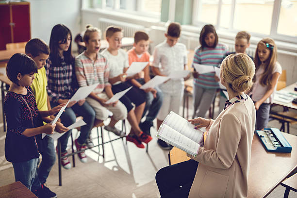 nauczyciel szkoły podstawowej śpiewa z dziećmi w klasie. - singing lesson zdjęcia i obrazy z banku zdjęć