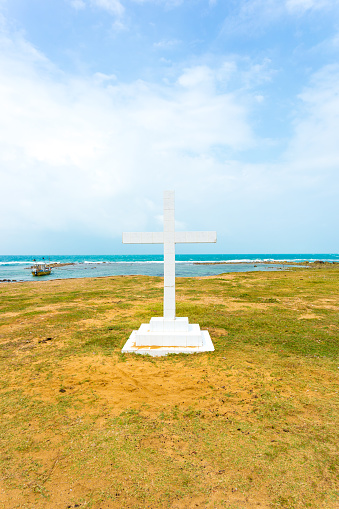 White cross is planted outside of Saint Thomas Church along the ocean in Point Pedro, Jaffna, Sri Lanka. Vertical