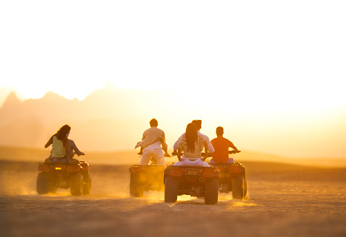 Adult man and woman dressed in arafatkas sit on quad bikes against the backdrop of stone mountains in the Echo Valley near Sharm El Sheikh, Egypt. Couple of tourists on ATVs in the Sinai Desert