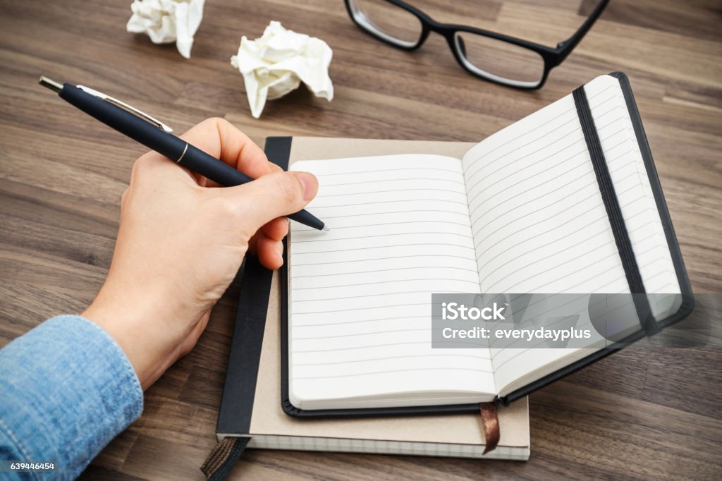 Woman hand writing on notebook Woman hand writing on notebook on wood desk with crumpled paper balls Left Handed Stock Photo