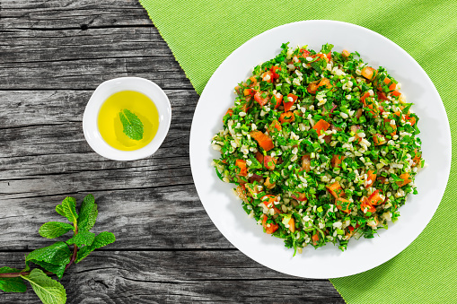 parsley salad or Tabbouleh on white platter, easy and healthy classic vegetarian dish with bulgur, tomatoes, parsley, spring onion and mint, olive oil on dark wooden background,view from above