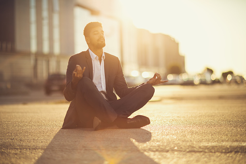 Young African American businessman sitting on the street and doing Yoga relaxation exercises.