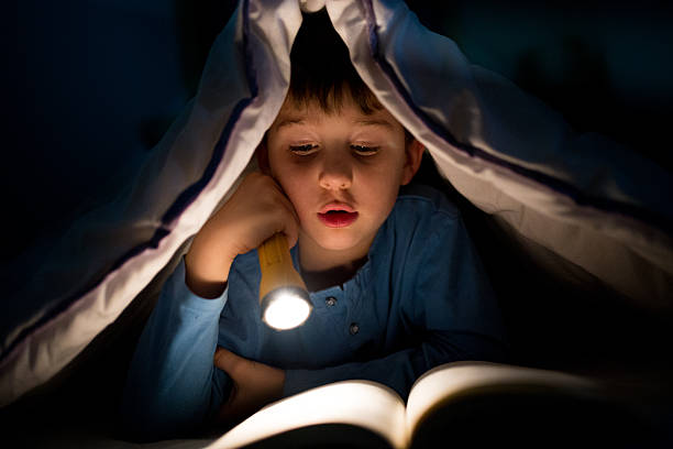 istock Little boy reading a book under the covers with flashlight 639454116