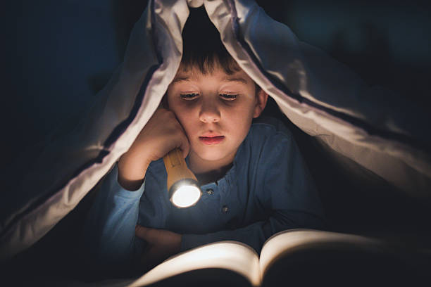 istock Little boy reading a book under the covers with flashlight 639454220